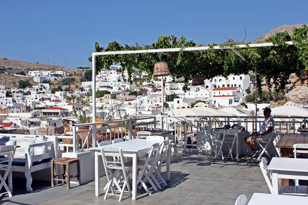 Blick von weiß möblierter Rooftop-Bar auf Lindos weißen Häuser, Ausflugstipp für Rhodos