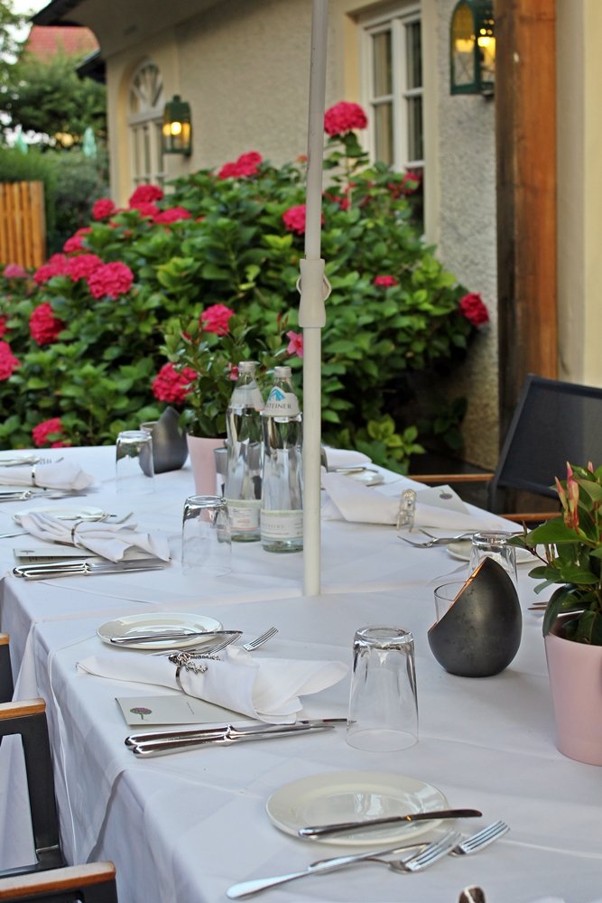 Hübsch gedeckter Tisch unter Sonnenschirm vor roten Hortensien, Hauben-Restaurant im Romantik Hotel GMACHL, Rezept Salzburger Nockerl