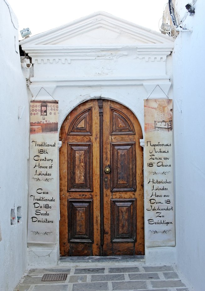 Eine braune Holztür mit Schrift auf einer weißen Wand in Lindos